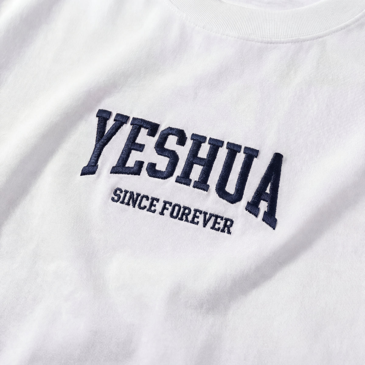 Närbild av marinblå broderad YESHUA – Since Forever-logotyp på vit t-shirt